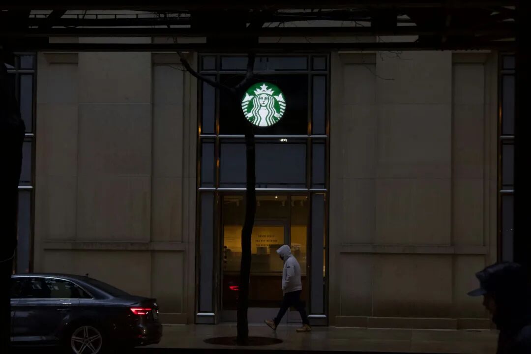 a man walking past a starbucks sign at night